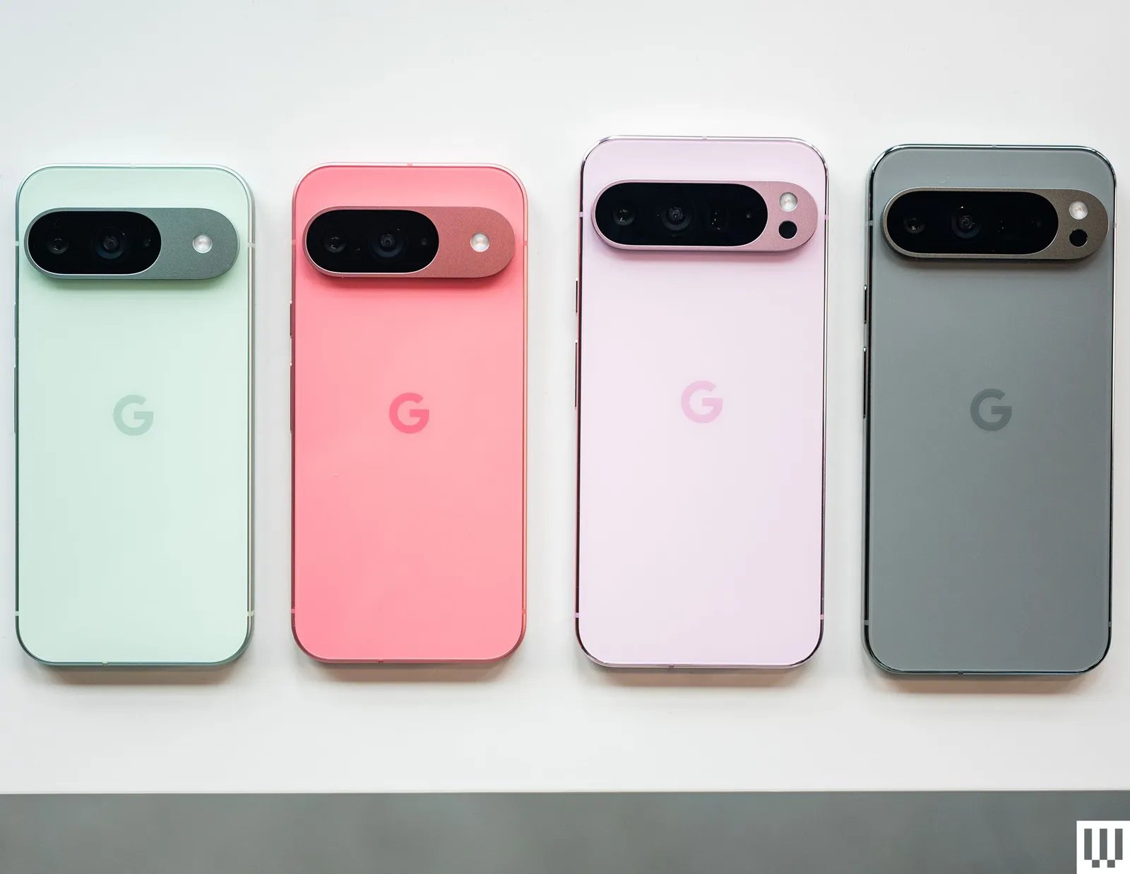 4 mobile phones face down camera side up side by side in teal pink light pink and grey .