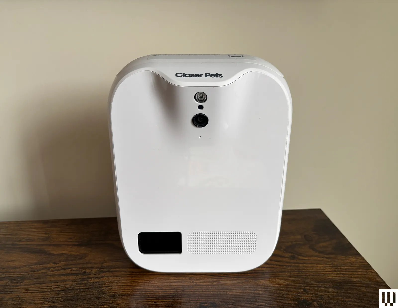 White rectangle treatdispensing pet camera sits on a wood ledge with cream wall background