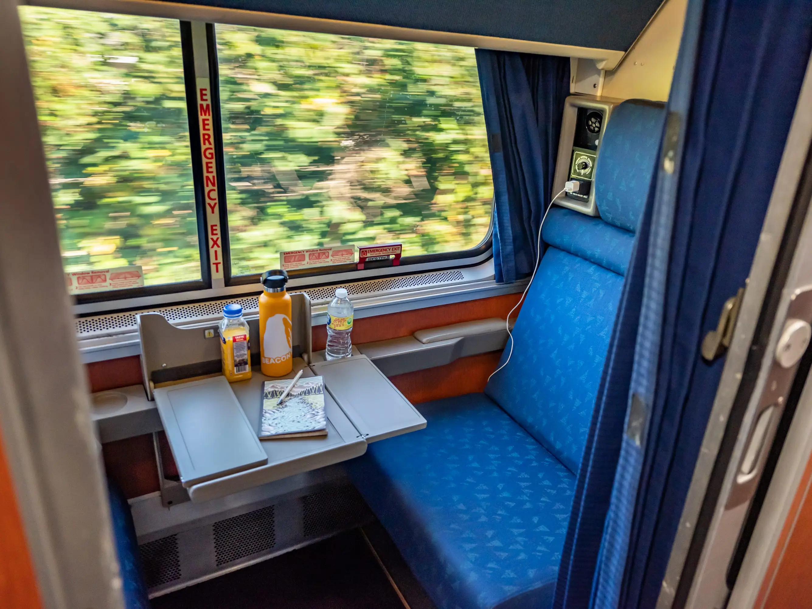 Train car with tray pulled out and blur of trees in window as train passes by