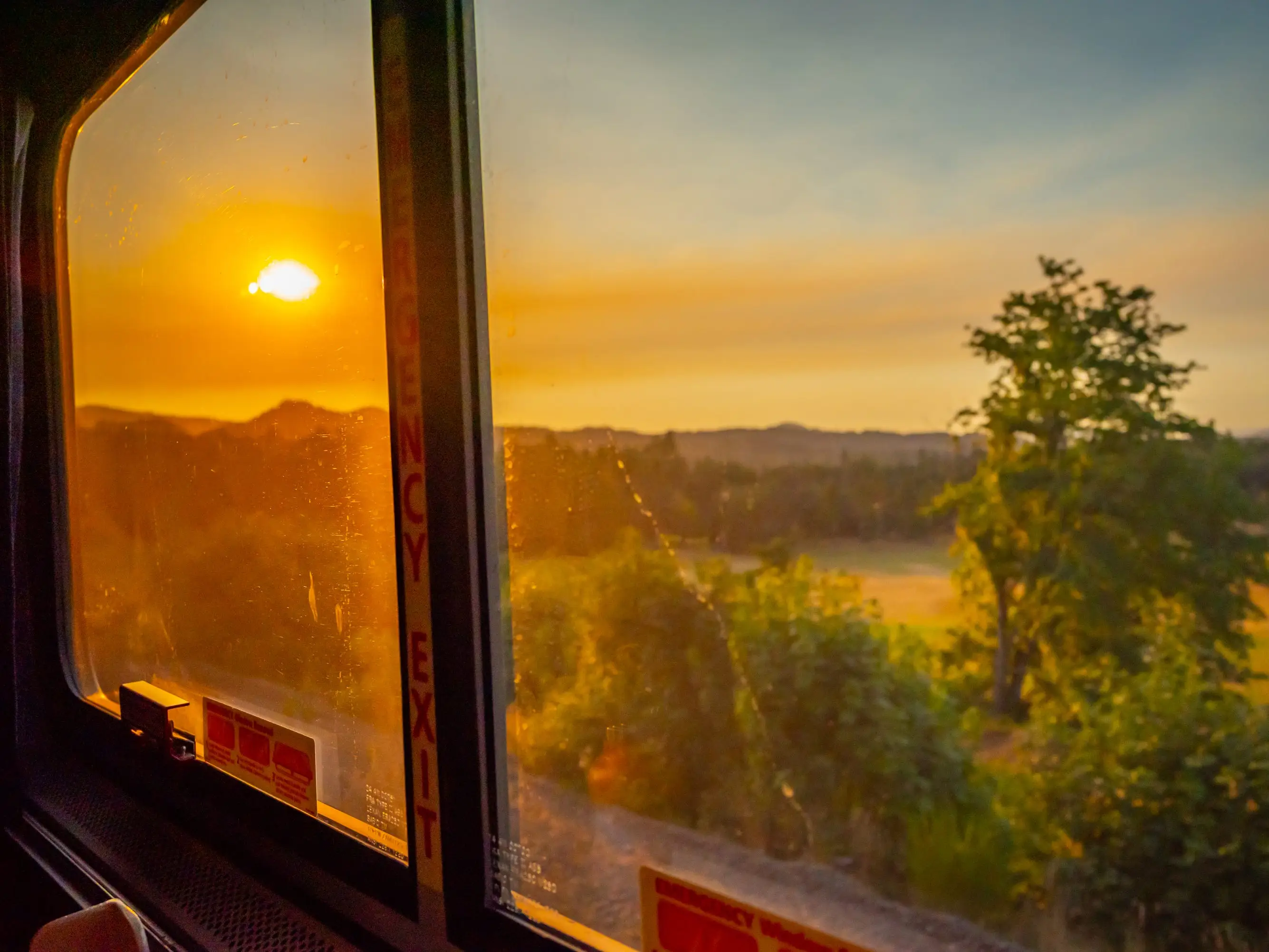 View of sunset against mountains and trees outside of Amtrak window
