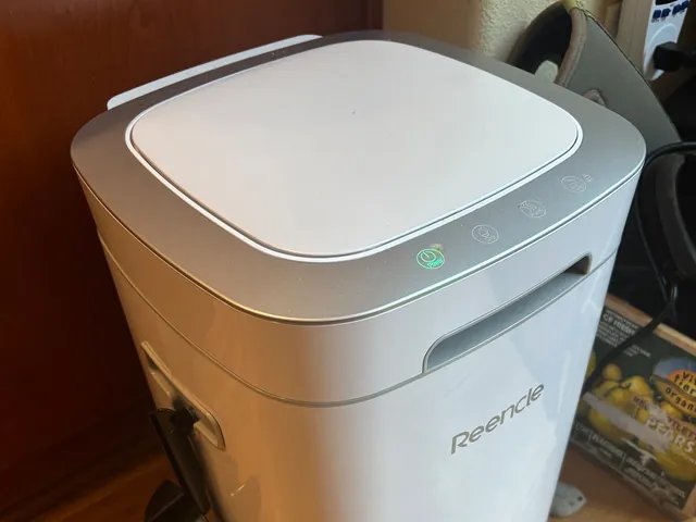 Side view of the Reencle Prime Electric Home Composter, a white rectangular device with a small black scooper attached to the side
