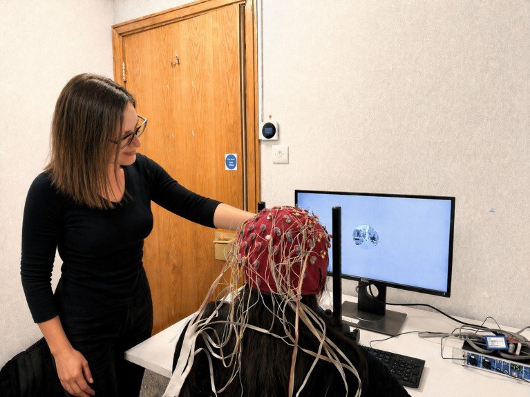 Nilli Lavie instructing a participant how to perform a computer based task, with the participant seated wearing an EEG cap.