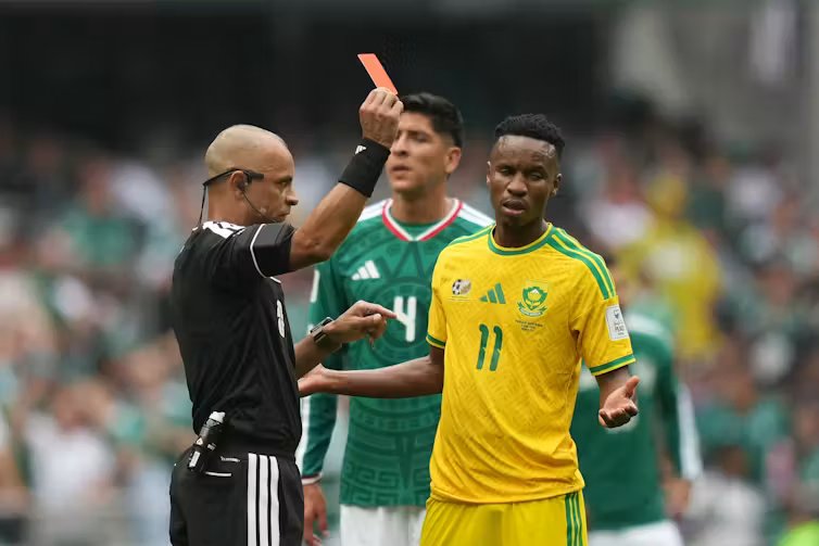 A man dressed in black holds aloft a red card.