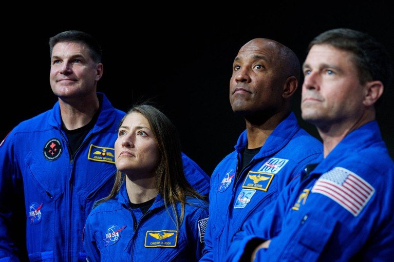 From left to right Artemis II crew Jeremy Hansen, Christina Koch, Victor Glover and Reid Wiseman look on while stood against a black background.