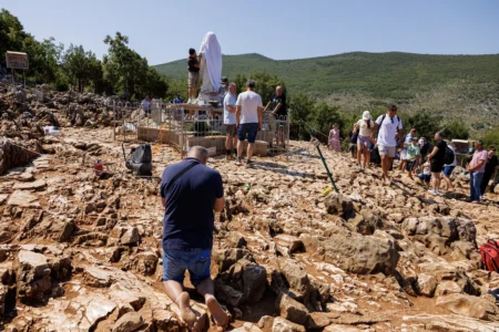 Pilgrims pray next to the vandalized statue of the Virgin Mary, which has been covered with a white sheet, on Apparition Hill in Medjugorje, Bosnia, Tuesday, July 28, 2026. (Credit: AP Photo/AP.)
