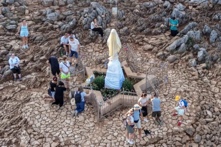 An aerial view of pilgrims praying next to the vandalized statue of the Virgin Mary, which has been covered with a white sheet, on Apparition Hill in Medjugorje, Bosnia, Tuesday, July 28, 2026. (Credit: AP Photo.)