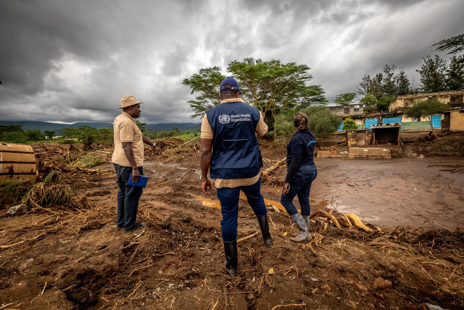 Man in WHO jacket and two other people looking over waterlogged ground